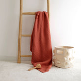 Terra cotta 4-ply muslin baby blanket hanging on wooden ladder with baby toys beside